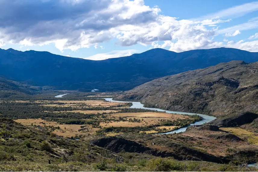 Wide valley with a winding river and rugged mountains under a bright sky in Patagonia, showcasing the landscapes often explored on Torres del Paine tours